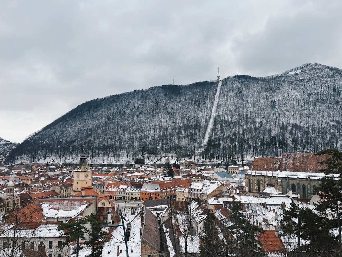 Snow on Brașov's Old Town rooftops, with the Council Square clock tower and the Black Church below a frost-covered Tâmpa