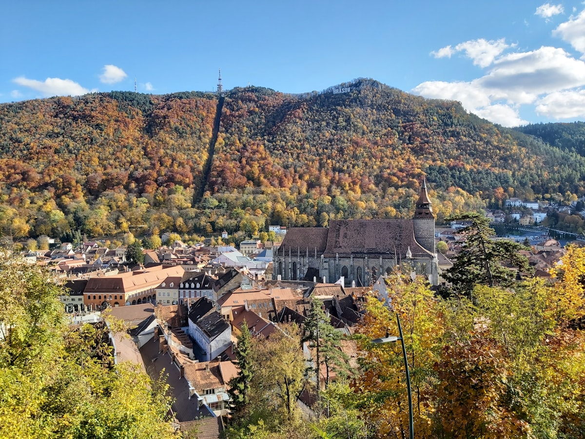 Brașov's Old Town and the Black Church below the wooded ridge of Tâmpa in autumn, with the cable-car line cut straight up the slope